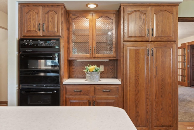 kitchen with brown cabinetry, light countertops, and glass insert cabinets