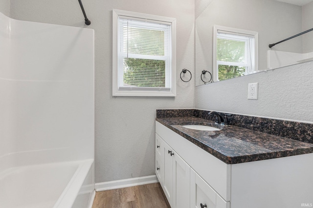 bathroom featuring wood finished floors, vanity, baseboards, and shower / washtub combination