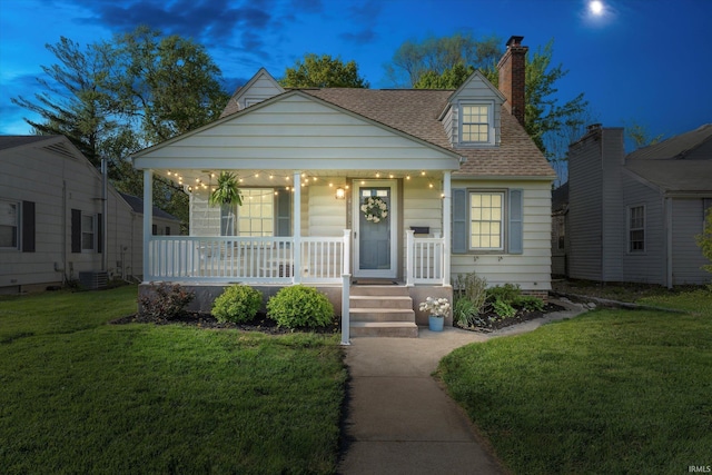 view of front of property with covered porch, roof with shingles, a front yard, and a chimney