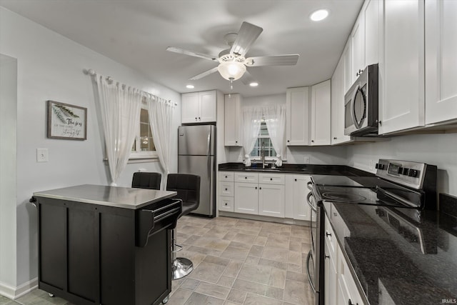 kitchen featuring appliances with stainless steel finishes, white cabinets, ceiling fan, recessed lighting, and dark stone countertops