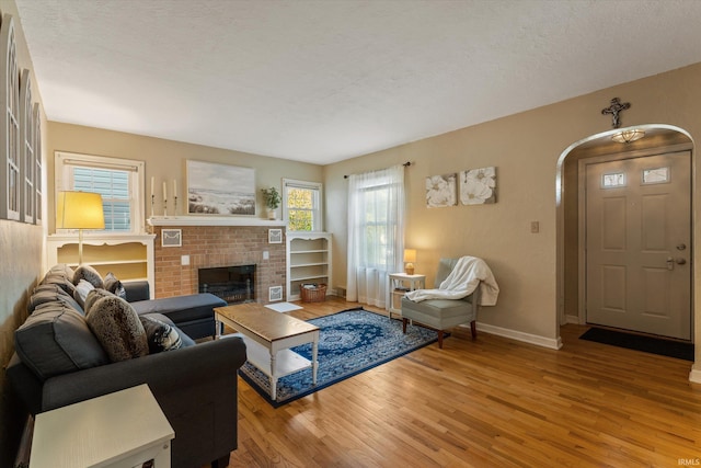 living area with light wood-style flooring, plenty of natural light, baseboards, a brick fireplace, and a textured ceiling