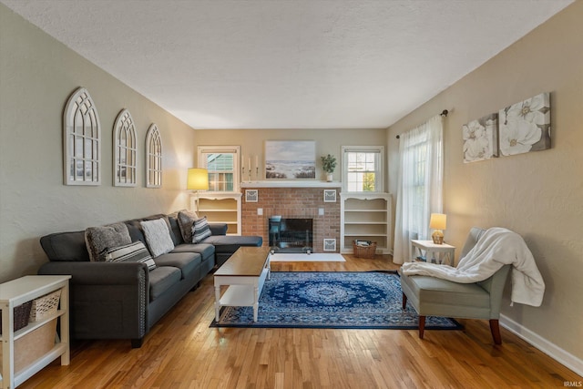 living room featuring hardwood / wood-style flooring, baseboards, a textured wall, a textured ceiling, and a brick fireplace