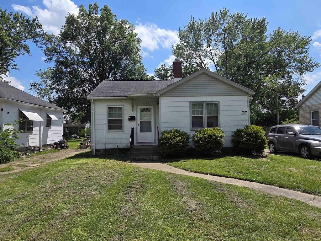 bungalow-style home featuring a chimney, a front yard, and roof with shingles