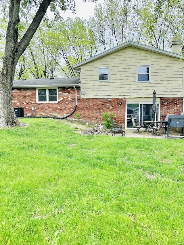 2912 W Twickingham Dr, Muncie, IN 47304 - rear view of house featuring brick siding, a chimney, a patio area, a yard, and central AC unit