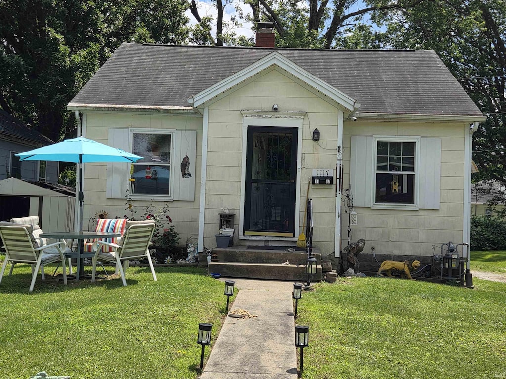 bungalow featuring a chimney, roof with shingles, and a front yard