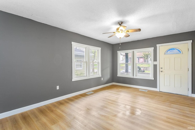 foyer entrance featuring light wood finished floors, baseboards, ceiling fan, and a textured ceiling