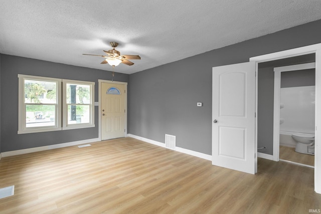 foyer entrance with light wood finished floors, a ceiling fan, baseboards, and a textured ceiling