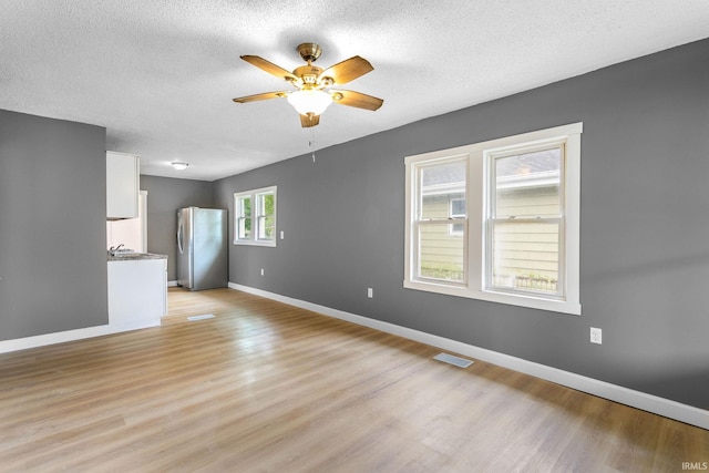 unfurnished living room featuring ceiling fan, light wood finished floors, baseboards, and a textured ceiling