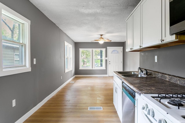 kitchen with stainless steel dishwasher, a sink, light wood finished floors, a textured ceiling, and baseboards
