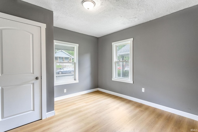empty room with plenty of natural light, light wood finished floors, baseboards, and a textured ceiling
