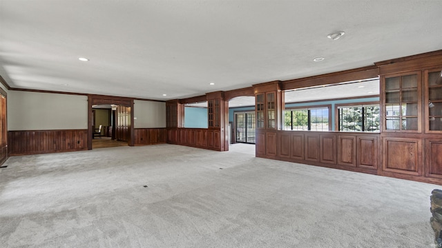 unfurnished living room featuring arched walkways, light colored carpet, wooden walls, a wainscoted wall, and recessed lighting