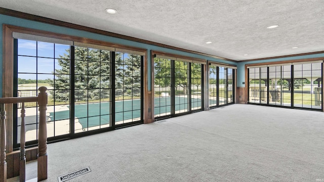 unfurnished living room with crown molding, plenty of natural light, a textured ceiling, carpet floors, and recessed lighting