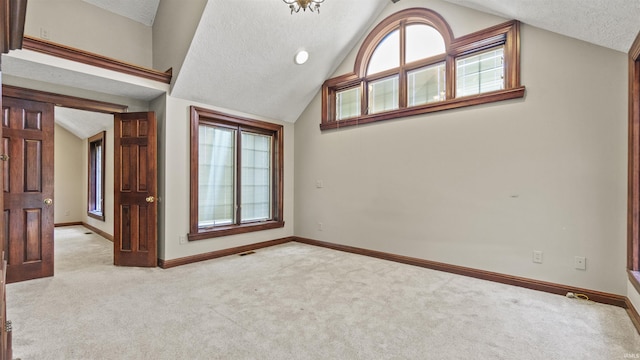 unfurnished room featuring lofted ceiling, light colored carpet, baseboards, and a textured ceiling
