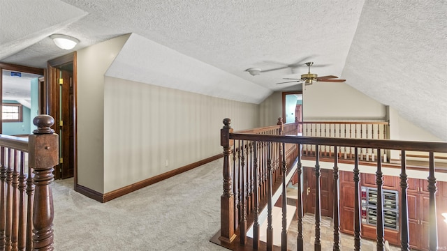 hall featuring an upstairs landing, a textured ceiling, baseboards, carpet flooring, and vaulted ceiling