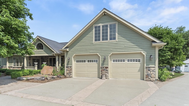view of front of home with stone siding, driveway, covered porch, and a garage