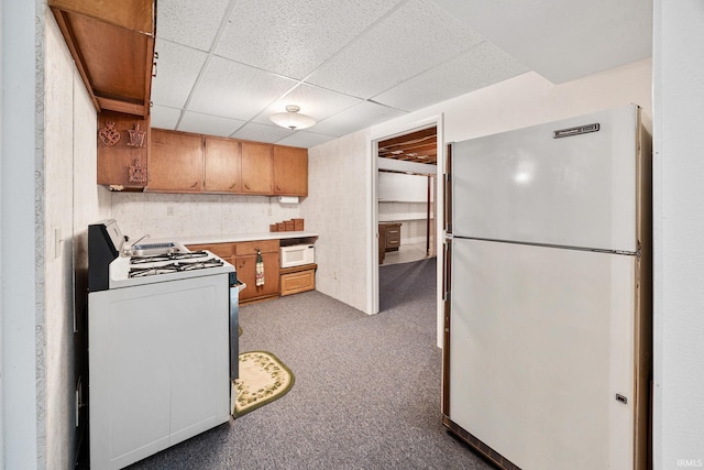 kitchen featuring white appliances, a paneled ceiling, carpet, brown cabinetry, and light countertops