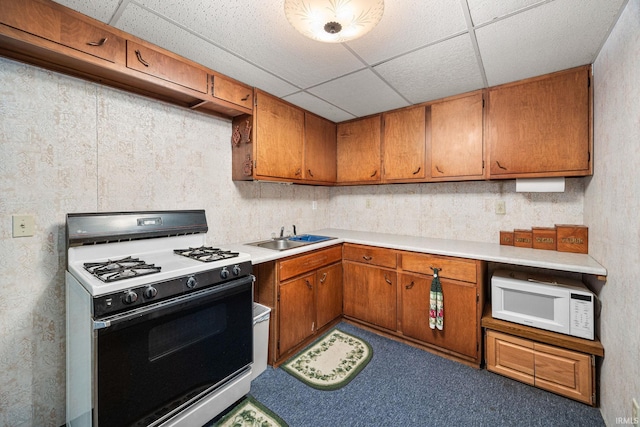 kitchen featuring gas range oven, white microwave, a sink, a drop ceiling, and brown cabinets