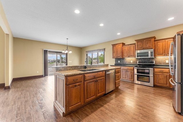 kitchen featuring stainless steel appliances, a sink, brown cabinets, a kitchen island with sink, and recessed lighting