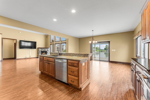 kitchen featuring stainless steel dishwasher, brown cabinets, light wood-type flooring, a chandelier, and a stone fireplace