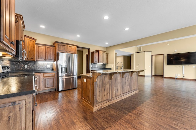 kitchen with appliances with stainless steel finishes, a kitchen breakfast bar, tasteful backsplash, dark wood finished floors, and recessed lighting