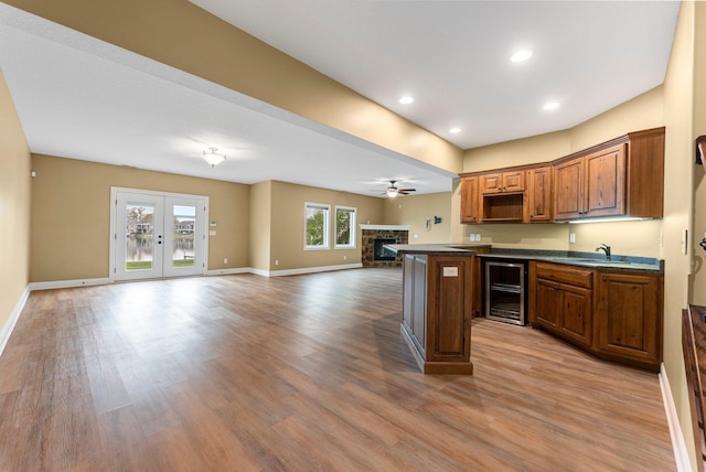 kitchen with beverage cooler, dark countertops, a stone fireplace, open floor plan, and light wood-style floors