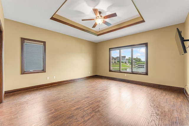 empty room with a tray ceiling, a ceiling fan, and wood finished floors