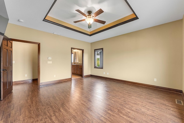 empty room featuring a tray ceiling, ceiling fan, dark wood-type flooring, and baseboards
