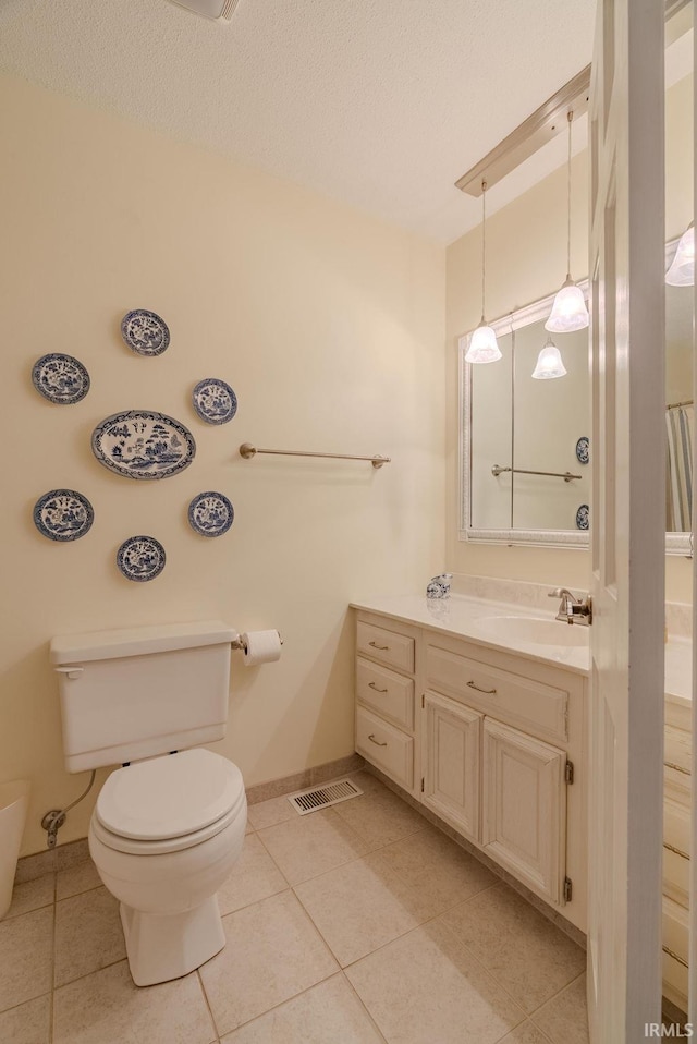 bathroom with toilet, tile patterned floors, vanity, baseboards, and a textured ceiling