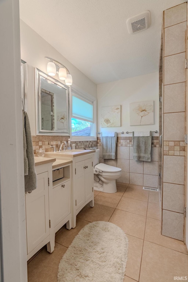 bathroom featuring tile walls, toilet, vanity, tile patterned floors, and a textured ceiling
