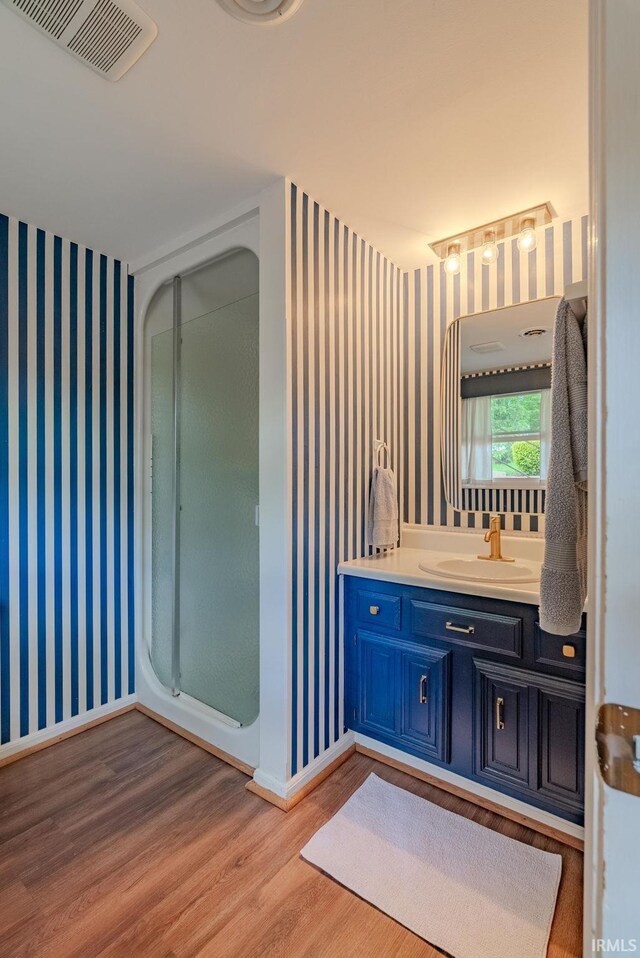bathroom featuring wood finished floors, wallpapered walls, a shower stall, vanity, and baseboards