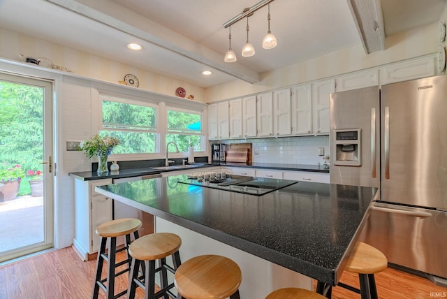 kitchen featuring stainless steel refrigerator with ice dispenser, black electric stovetop, a sink, dark countertops, and white cabinets