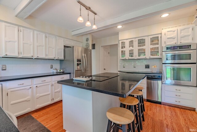 kitchen featuring stainless steel appliances, white cabinets, a kitchen bar, backsplash, and recessed lighting