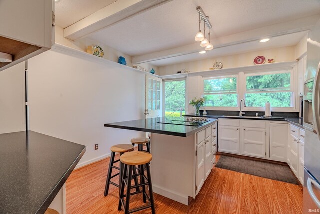 kitchen with a sink, black electric stovetop, white cabinets, a breakfast bar, and light wood finished floors