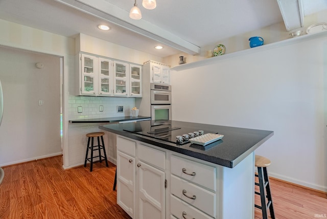 kitchen featuring a breakfast bar, black electric stovetop, stainless steel double oven, dark countertops, and decorative backsplash