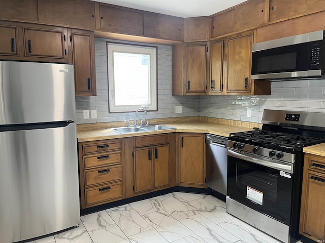kitchen featuring stainless steel appliances, a sink, light countertops, and light marble finish flooring