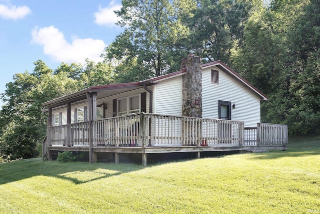 rear view of property with a chimney, a lawn, and a wooden deck