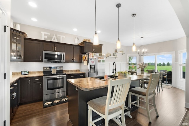 kitchen with appliances with stainless steel finishes, a sink, dark wood-style flooring, decorative backsplash, and a kitchen bar