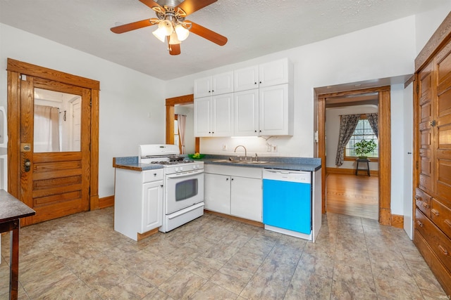 kitchen featuring white range with gas stovetop, dishwashing machine, a sink, dark countertops, and white cabinets
