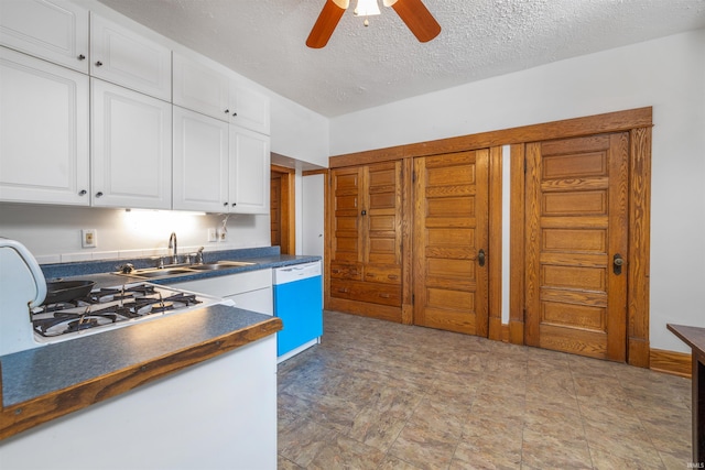 kitchen featuring dark countertops, dishwashing machine, a sink, white cabinets, and a ceiling fan