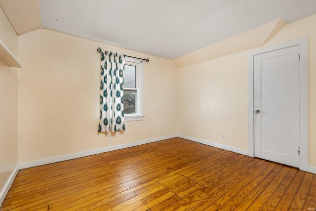 spare room with vaulted ceiling, wood-type flooring, and baseboards