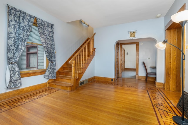 unfurnished living room featuring wood finished floors, arched walkways, stairway, and baseboards