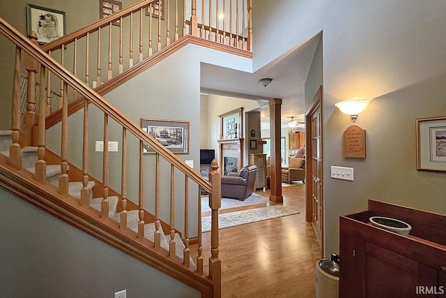 staircase with a towering ceiling, decorative columns, wood finished floors, and a glass covered fireplace