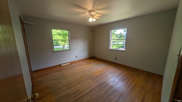 empty room with healthy amount of natural light, wood finished floors, a ceiling fan, and baseboards