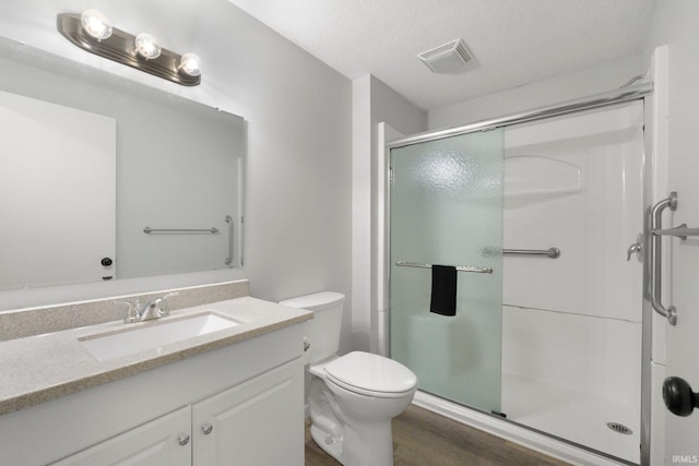 full bathroom featuring a stall shower, toilet, wood finished floors, vanity, and a textured ceiling