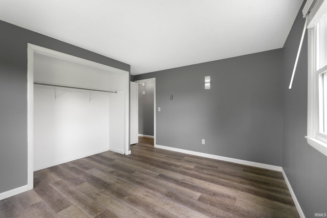 unfurnished bedroom with dark wood-style flooring, a closet, and baseboards