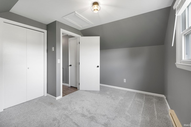 unfurnished bedroom featuring a baseboard heating unit, vaulted ceiling, carpet flooring, attic access, and baseboards