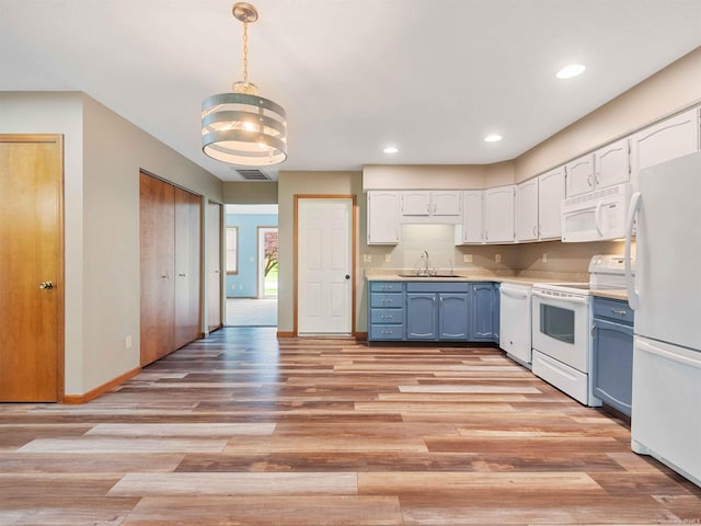 kitchen with white appliances, blue cabinets, a sink, light countertops, and light wood-type flooring
