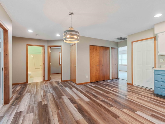 unfurnished bedroom featuring two closets, wood finished floors, baseboards, recessed lighting, and a chandelier