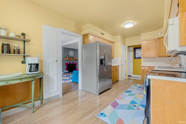 kitchen featuring stainless steel fridge with ice dispenser, white microwave, light countertops, light wood-style flooring, and a sink