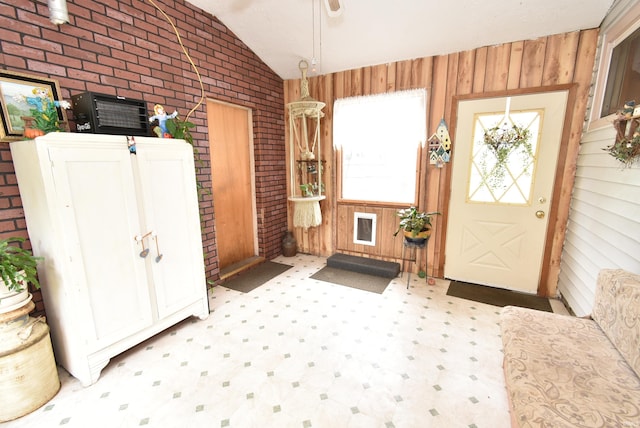 entryway featuring tile patterned floors, wood walls, vaulted ceiling, and brick wall